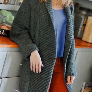 May include: A long-sleeved, dark green cardigan with a wide collar. The cardigan is made of a soft, textured fabric and is open in the front.