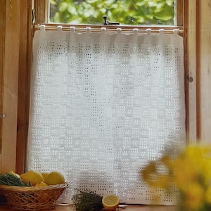 May include: White crocheted curtain hanging in a window with a view of green trees outside. A basket of lemons and a lemon on a wooden surface are in the foreground.