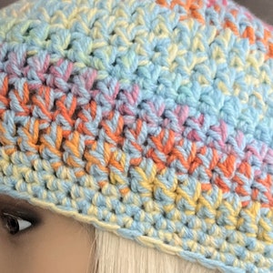 May include: A crocheted hat in a rainbow color pattern of light blue, yellow, pink, and orange. The hat is made with a single crochet stitch.