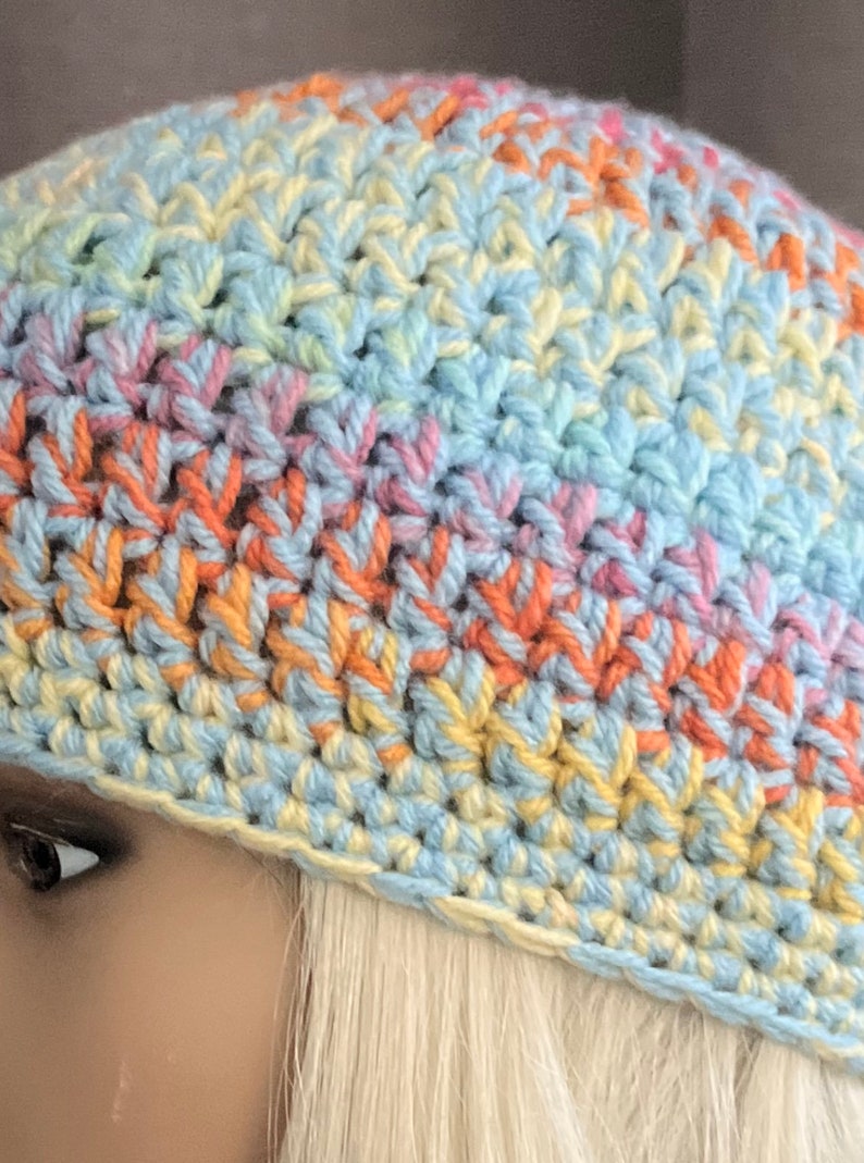 May include: A crocheted hat in a rainbow color pattern of light blue, yellow, pink, and orange. The hat is made with a single crochet stitch.