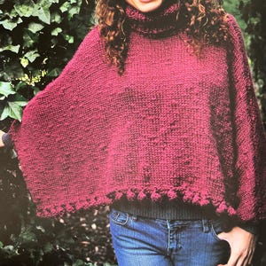 May include: A maroon knitted poncho with a turtleneck and a textured design. The poncho has a scalloped hem with small pom-poms.