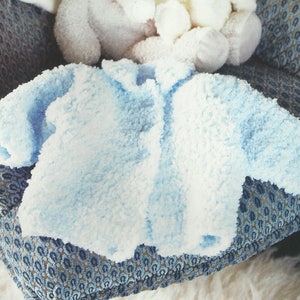 May include: A light blue knitted baby jacket with a fuzzy texture.