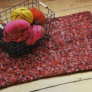 Peut inclure: Des pelotes de laine rouge, rose, jaune et verte sont dans un panier en fil de fer noir. Le panier est sur un tapis tricoté rouge et blanc.