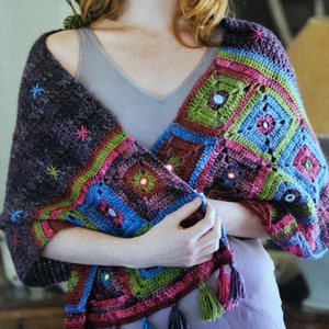May include: A colorful crocheted shawl with a geometric pattern and mirrored accents. The shawl is made with a variety of colors, including purple, pink, green, blue, and brown. The shawl is fringed on the edges.