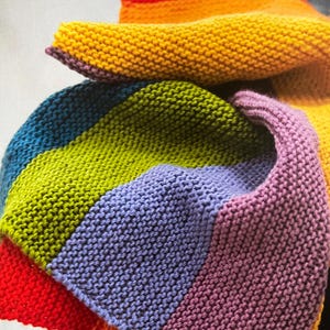 May include: A rainbow striped knitted blanket with red, orange, yellow, green, blue and purple stripes.