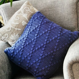 May include: A blue knitted cushion with a textured surface sits on a grey sofa.