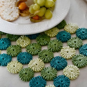 May include: A crocheted table runner with a repeating pattern of green, teal, and cream circles. The runner is made with a textured yarn and has a delicate, feminine look.