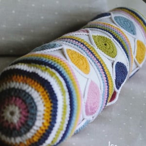 May include: A colorful crocheted pillow with a geometric pattern of circles and teardrop shapes. The pillow is made with white, pink, yellow, blue, and green yarn.