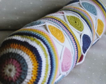 May include: A colorful crocheted pillow with a geometric pattern of circles and teardrop shapes. The pillow is made with white, pink, yellow, blue, and green yarn.