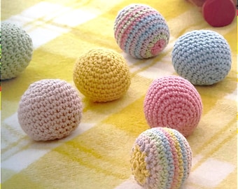 May include: Six crocheted balls in various pastel colors, including pink, yellow, blue, and green. The balls are arranged on a yellow and white checkered surface.