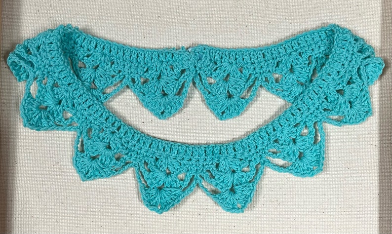 May include: A teal crocheted collar with a scalloped edge. The collar is made of delicate crochet stitches and has a lacy appearance.