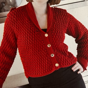 May include: A red crocheted cardigan with a wide collar and gold buttons. The cardigan is cropped and has a textured stitch pattern.