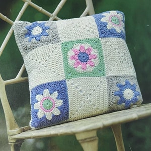 May include: A crocheted pillow with a patchwork design featuring blue, green, and pink flowers. The pillow is made of white yarn and has a square shape.
