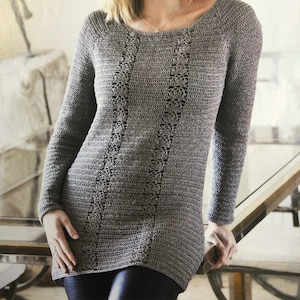 Può includere: Un maglione di uncinetto grigio con un delicato motivo a pizzo. Il maglione ha maniche lunghe e una scollatura rotonda.