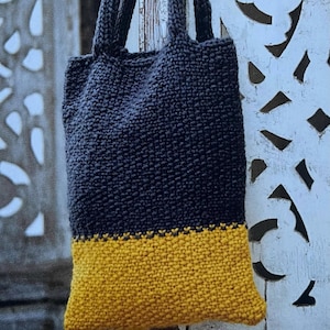 Op de afbeelding: Handgemaakte draagtas in een tweekleurig ontwerp. Het bovenste gedeelte is donker marineblauw, dat overgaat in een mosterdgele basis. De tas is gemaakt van een dik, getextureerd gebreid materiaal met bijpassende marineblauwe handvatten.