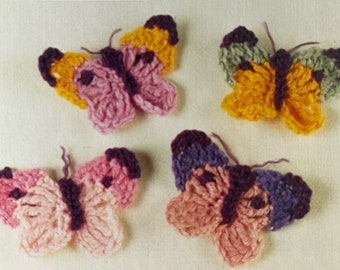 May include: Four crocheted butterflies in different colors: pink, purple, yellow, and green. The butterflies have dark purple accents and are made with a textured stitch.