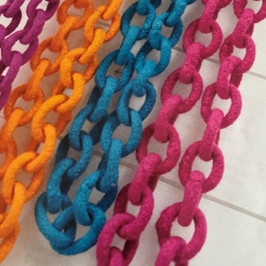 May include: Close-up of colorful, felt-covered chain links in shades of purple, orange, blue, and pink. The chains are arranged in parallel rows, creating a vibrant and textured pattern. The felt adds a soft, tactile quality to the bold colors.