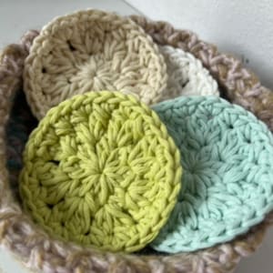 May include: Four crocheted cotton rounds in a basket. The rounds are in shades of beige, light green, and light blue.