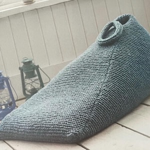 May include: A blue knitted beanbag chair with a loop handle. The beanbag is sitting on a wooden floor.