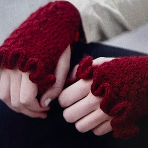 Peut inclure: Une paire de mitaines rouge cramoisi faites à la main. Les gants sont tricotés avec un point texturé et présentent un bord à volants autour du poignet. Les gants sont conçus pour garder les mains au chaud tout en laissant les doigts libres.
