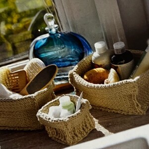 May include: Four small woven baskets with various items inside, including a blue glass bottle, a wooden brush, a white washcloth, and toiletries. The baskets are on a wooden surface.