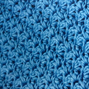 May include: Close-up of a blue crocheted fabric with a textured surface.