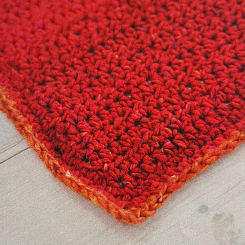 May include: Close-up of a red crocheted square with a brown border. The crocheted fabric has a textured, bumpy surface.