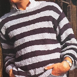 May include: A striped jumper with alternating black and light grey horizontal stripes. The jumper has a crew neck and long sleeves.
