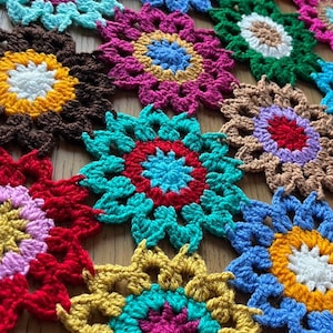 Peut inclure: Gros plan sur une couverture au crochet faite de carrés en forme de fleurs multicolores. La couverture est faite de différentes couleurs, notamment le rouge, le bleu, le jaune, le vert et le rose.