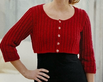 May include: A red knitted cropped cardigan with a button-up front and long sleeves. The cardigan has a ribbed texture and is a classic style.