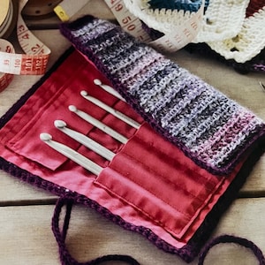 Puede incluir: Una funda de ganchillo morada con forro de satén rojo contiene un juego de seis agujas de ganchillo plateadas.