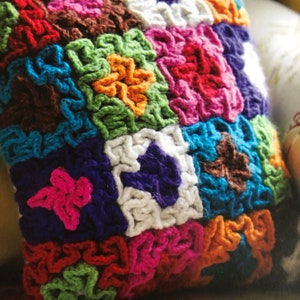 Puede incluir: Una almohada de crochet colorida con un diseño de patchwork que presenta cuadrados de diferentes colores, incluyendo rojo, rosa, azul, verde, naranja y marrón.