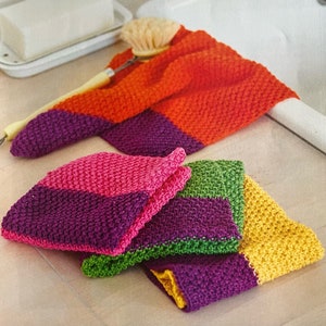 May include: Four knitted dishcloths in a variety of colours, including orange, pink, green, and yellow. The dishcloths are folded and stacked on a wooden surface.