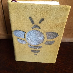 May include: A yellow suede journal with a silver glitter bee design.