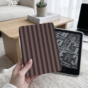 May include: A brown and tan striped Kindle cover is held in front of a Kindle device. The cover has vertical stripes. The Kindle is on a white surface. The text "Eternal Creative Arts" is in the upper left corner.