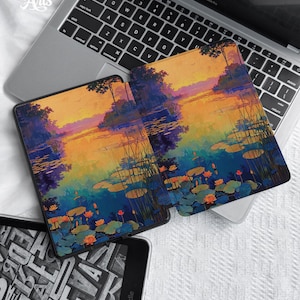 May include: Two Kindle covers and a laptop with the text "Eternal Creative Arts". The covers display a colourful landscape painting of a lake with lily pads, trees, and a sunset. The laptop is a MacBook Pro.