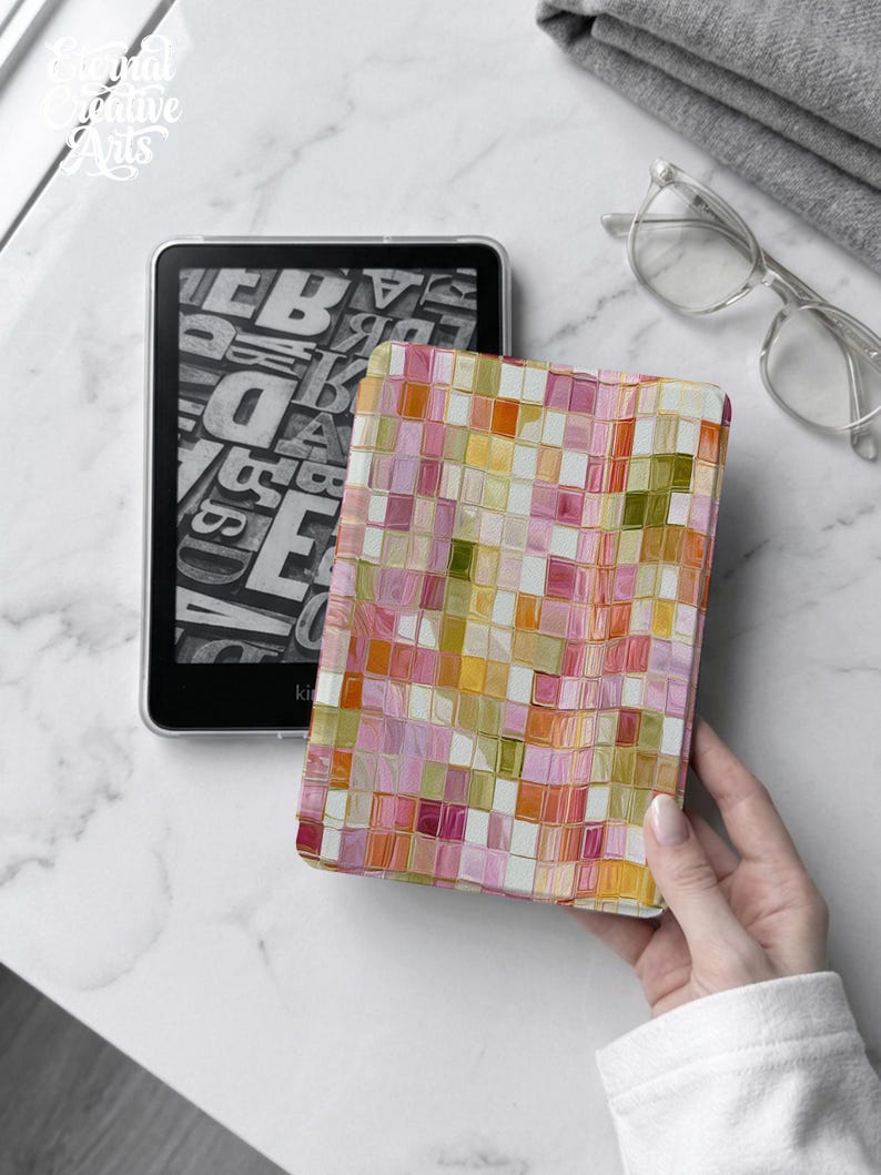 May include: An e-reader device featuring a black screen with a white typographic letter pattern. The device is encased in a protective cover displaying a vibrant mosaic of small, square tiles in shades of pink, orange, yellow, and olive green.