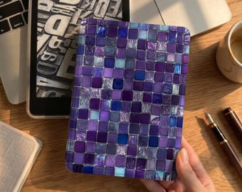 May include: A rectangular e-reader case featuring a vibrant mosaic pattern of small square tiles in various shades of purple, violet, and deep blue. The surface has a glossy finish that reflects light, creating a textured appearance across the grid.
