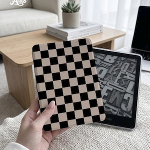 May include: A black and tan checkerboard pattern Kindle case is held in front of a Kindle device. The case is a hard shell with a repeating pattern of black and tan squares. The text "Eternal Creative Arts" is in the upper left corner.