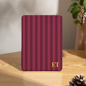 May include: A rectangular case with a vertical striped pattern in shades of burgundy and maroon. The initials "ET" are in gold on the lower right corner. The case is on a wooden surface.