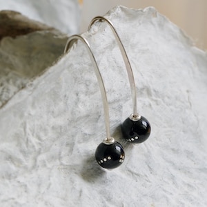 Peut inclure: Une paire de boucles d'oreilles pendantes en argent avec des perles sphériques noires. Chaque perle a un motif de points blancs.