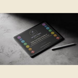 May include: A black tablet displaying the text "DIVINE VIBES HOUSE" and "THE SACRED ENERGY A Chakra & Subtle Body Journal". The tablet is surrounded by colorful chakra symbols and a white stylus rests beside it. The background is a textured gray surface.