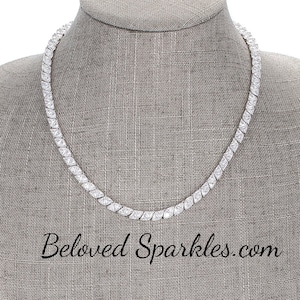 May include: A silver necklace with a row of clear cubic zirconia stones. The necklace is on a mannequin bust.