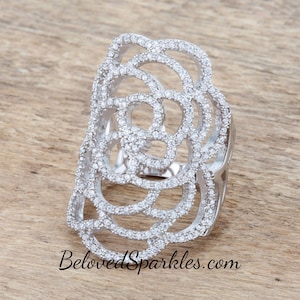 Pode incluir: Um anel de prata com um grande design vazado que se assemelha a uma rosa. O anel é adornado com pequenas pedras de zircônia cúbica transparentes.