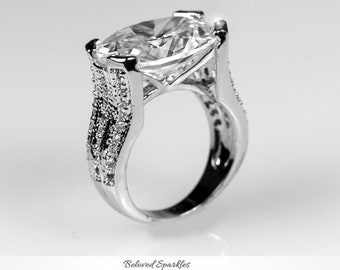 May include: A silver ring with a large, clear, oval-shaped gemstone set in a prong setting. The band of the ring is decorated with smaller gemstones.