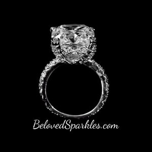 Op de afbeelding: Een grote, glinsterende, ronde diamanten verlovingsring met een zilveren band. De ring is geplaatst op een zwarte achtergrond.