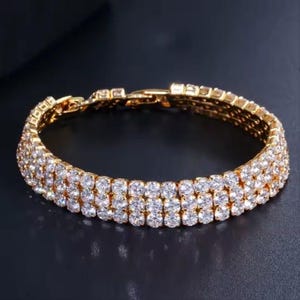 Puede incluir: Una pulsera de oro con tres filas de piedras de circonita cúbica transparentes.