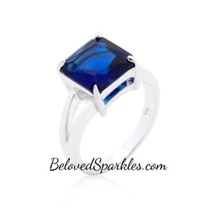 May include: A silver ring with a large, square-shaped, dark blue gemstone. The ring has a simple band with a delicate design.