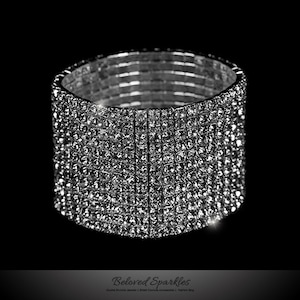 May include: A silver bracelet with multiple rows of clear rhinestones. The bracelet is made of metal and has a flexible design.