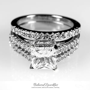 Puede incluir: Un anillo de compromiso de plata con un gran diamante de talla cojín y dos bandas de diamantes más pequeñas.